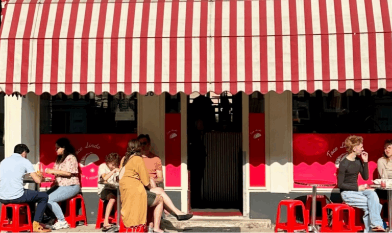 Mensen eten buiten onder een rood-wit gestreepte luifel.