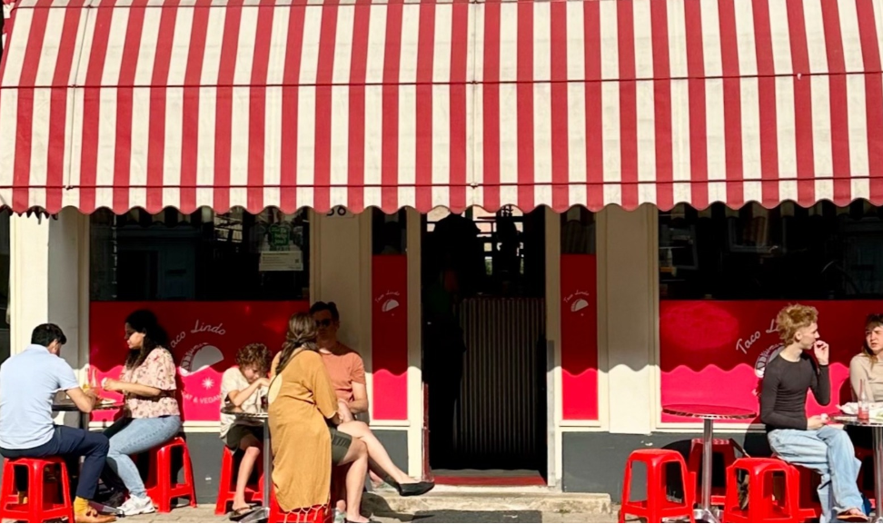 Mensen eten buiten onder een rood-wit gestreepte luifel.